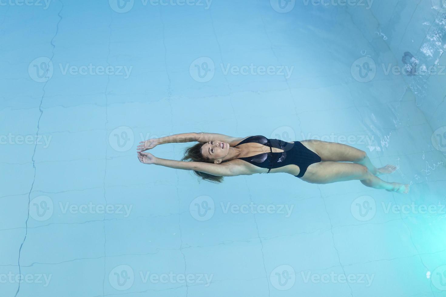 Top view aerial photo from flying drone of a seductive sexy model in white swimwear is enjoying relax in hotel pool during her summer weekend. Amazing fashion woman in bikini having luxury spa rest