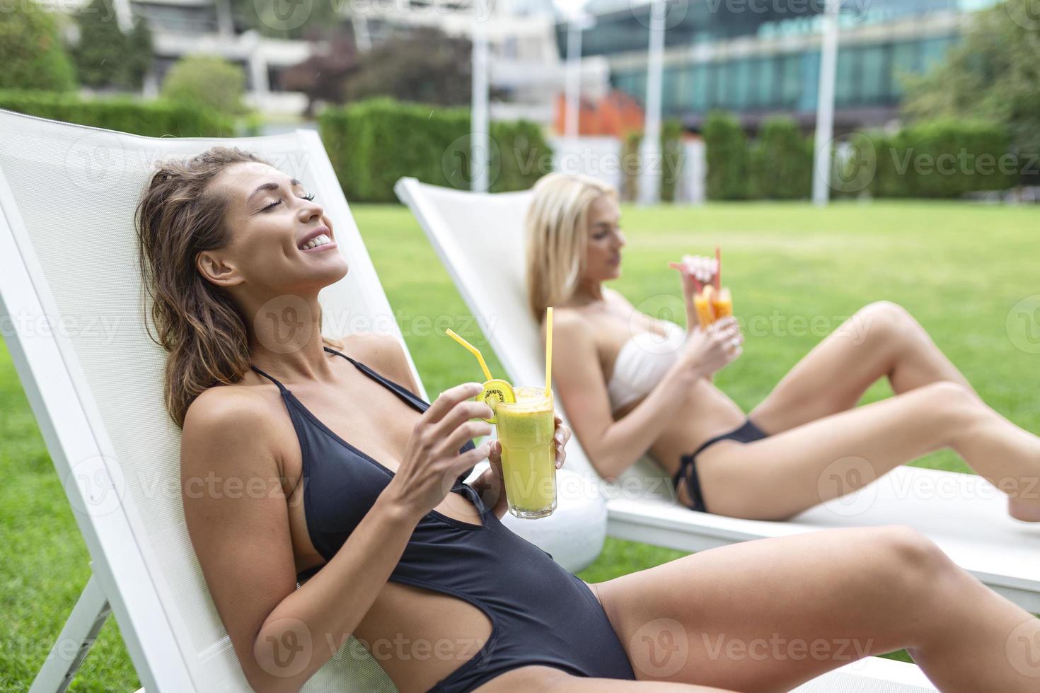 Beautiful women sunbathing, drinking cocktail, lying near swimming pool. Summer holidays and vacation photo