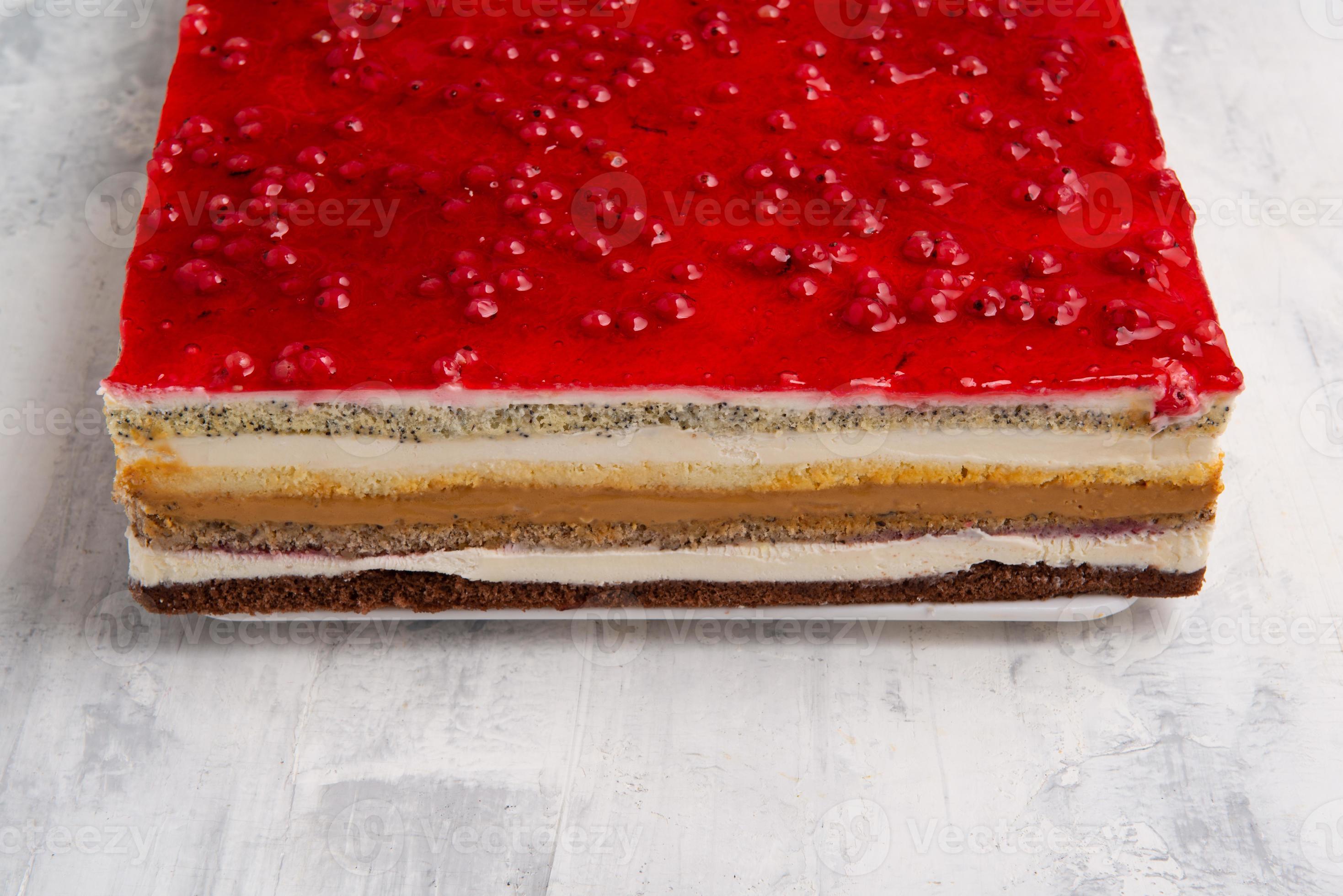An angle shot of a multilayered cake with a red currant jelly layer on