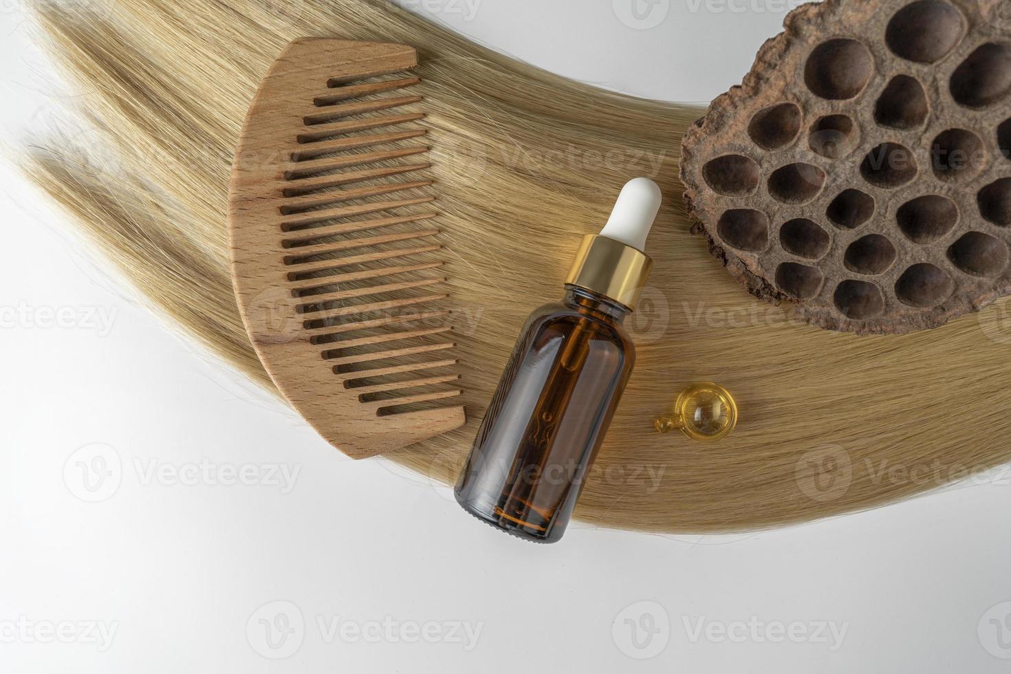 A hair care oil or serum in a brown dropper bottle and golden capsules lying on a blond hair strand, product marketing mockup photo