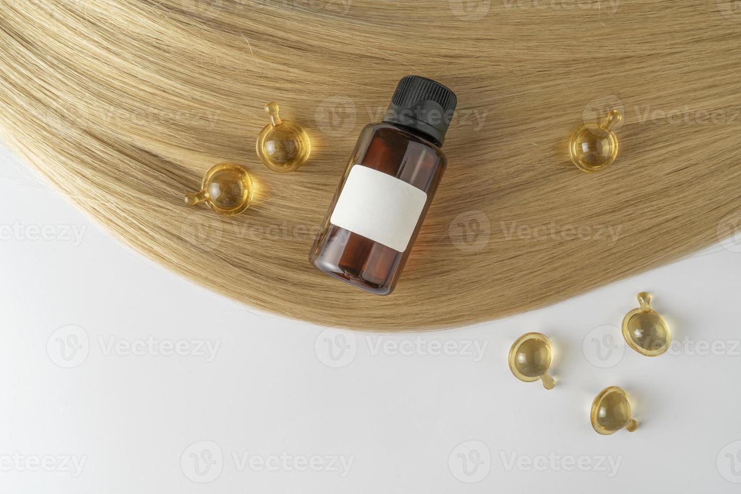 A hair care oil or serum in brown dropper bottles and golden capsules lying on a blond hair strand, product marketing mockup photo