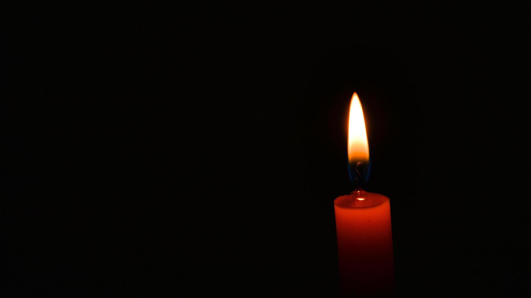 Burning orange candle flame in darkness copy space concept peace hope religion serenity photo