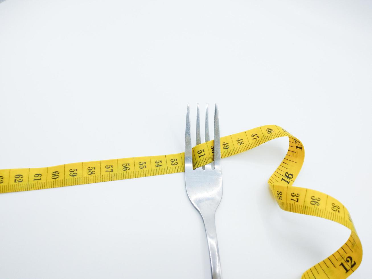 tenedor plateado con cinta métrica amarilla envuelta alrededor. sobre un fondo blanco, concepto, control de la dieta, pérdida de peso, estilo de vida saludable foto