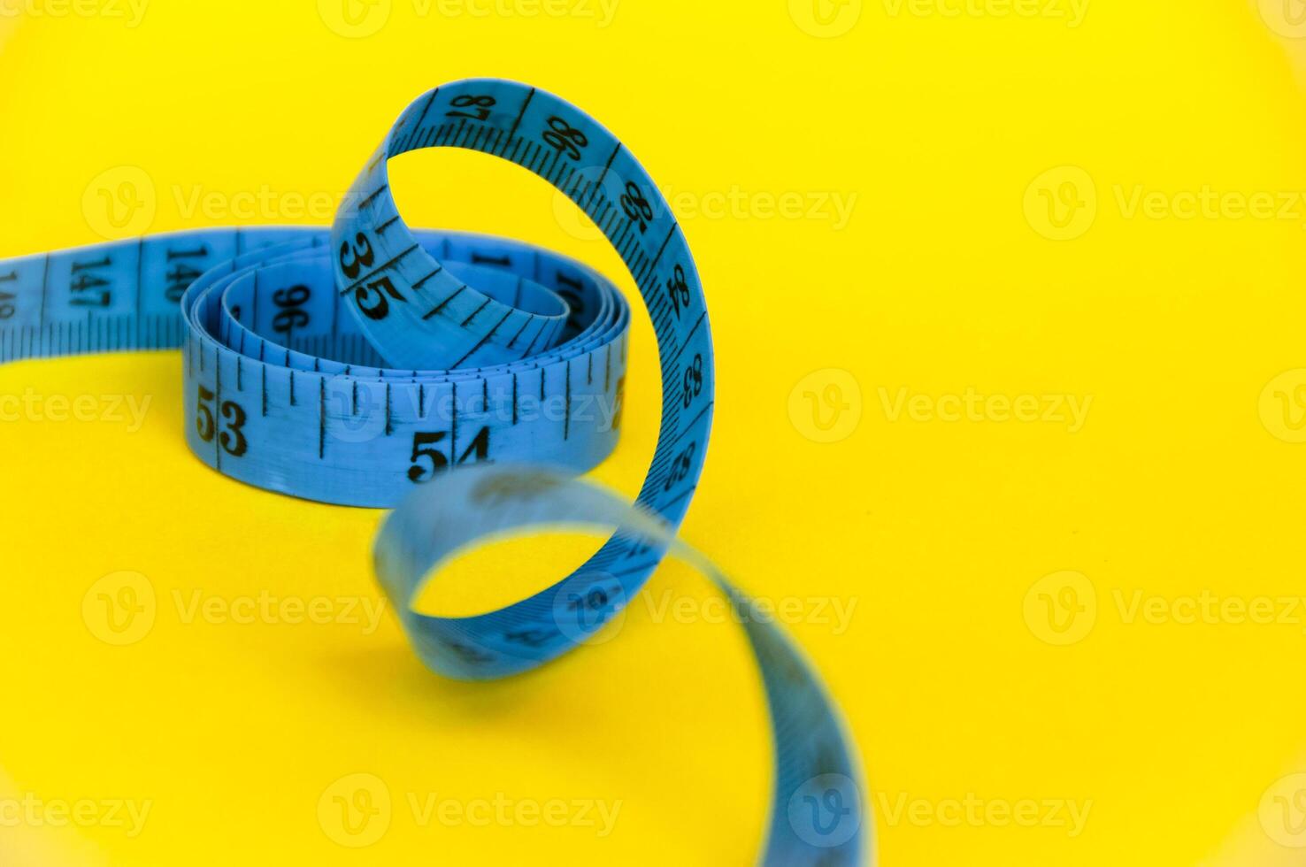 Top view of yellow soft measuring tape. Minimalist flat lay image of tape  measure with metric scale over turquoise blue background with copy space.  Stock Photo