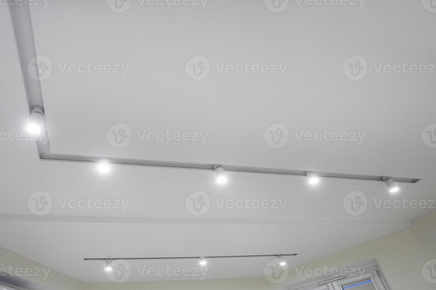 suspended ceiling with halogen spots lamps and drywall construction in empty room in apartment or house. Stretch ceiling white and complex shape. photo