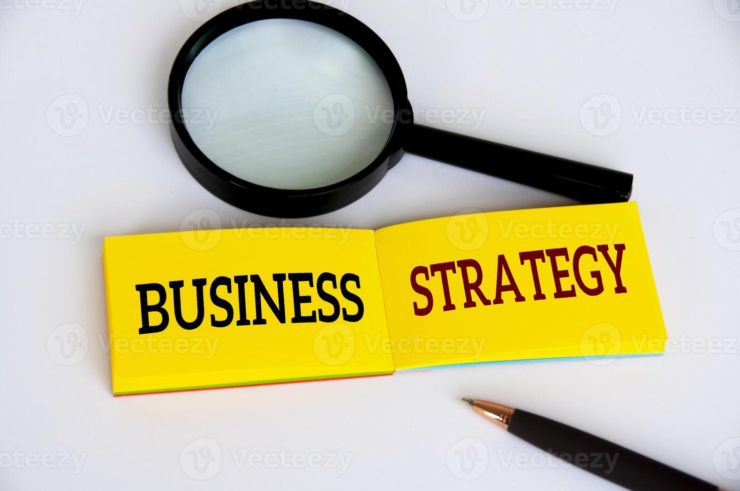 Business strategy text on yellow notepad with magnifying glass and pen on white background. Business strategy concept photo