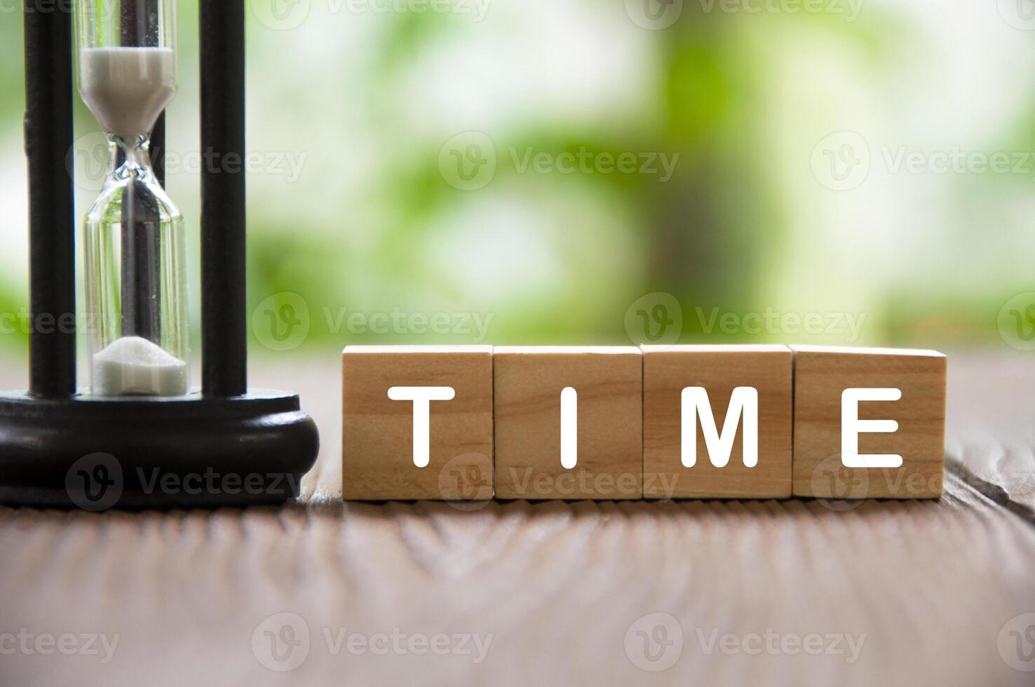 Time text on wooden blocks with minute glass and blurred nature background. Time concept photo