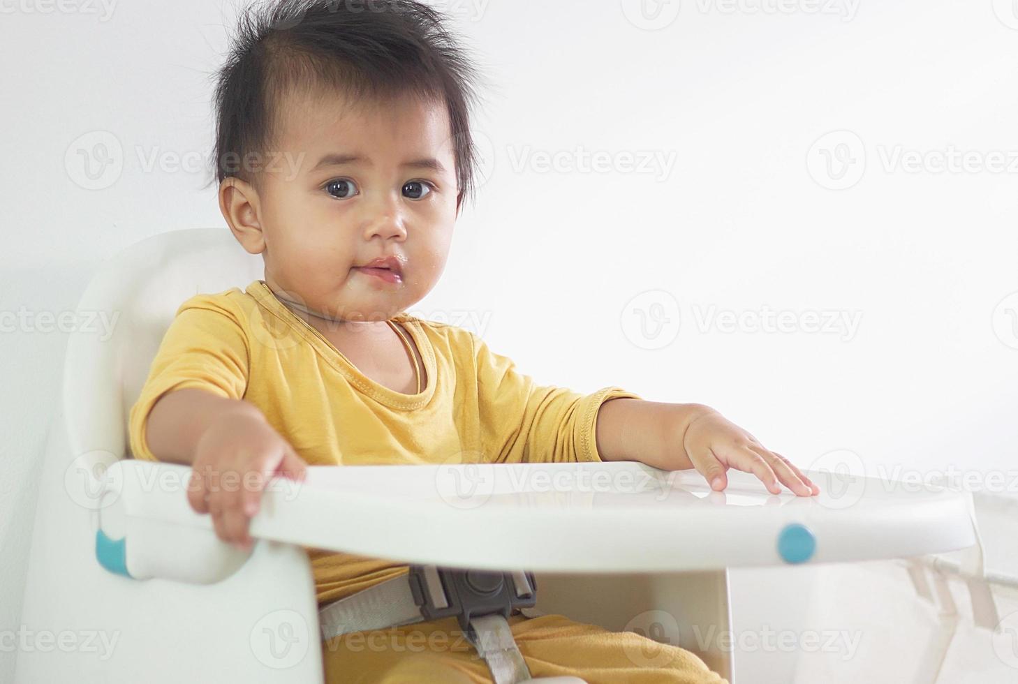 una linda chica blanca sentada en una silla desayunando en el hogar interior alimentando deliciosas comidas que son altamente nutritivas el bebé tiene una cara alegre, divertida, sonriente y feliz en un estilo de vida familiar saludable. foto