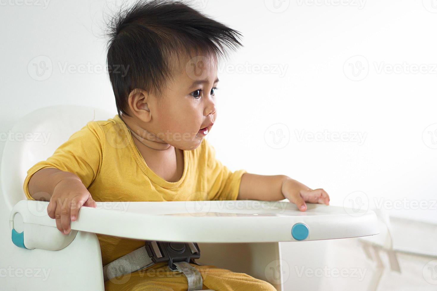 una linda chica blanca sentada en una silla desayunando en el hogar interior alimentando deliciosas comidas que son altamente nutritivas el bebé tiene una cara alegre, divertida, sonriente y feliz en un estilo de vida familiar saludable. foto