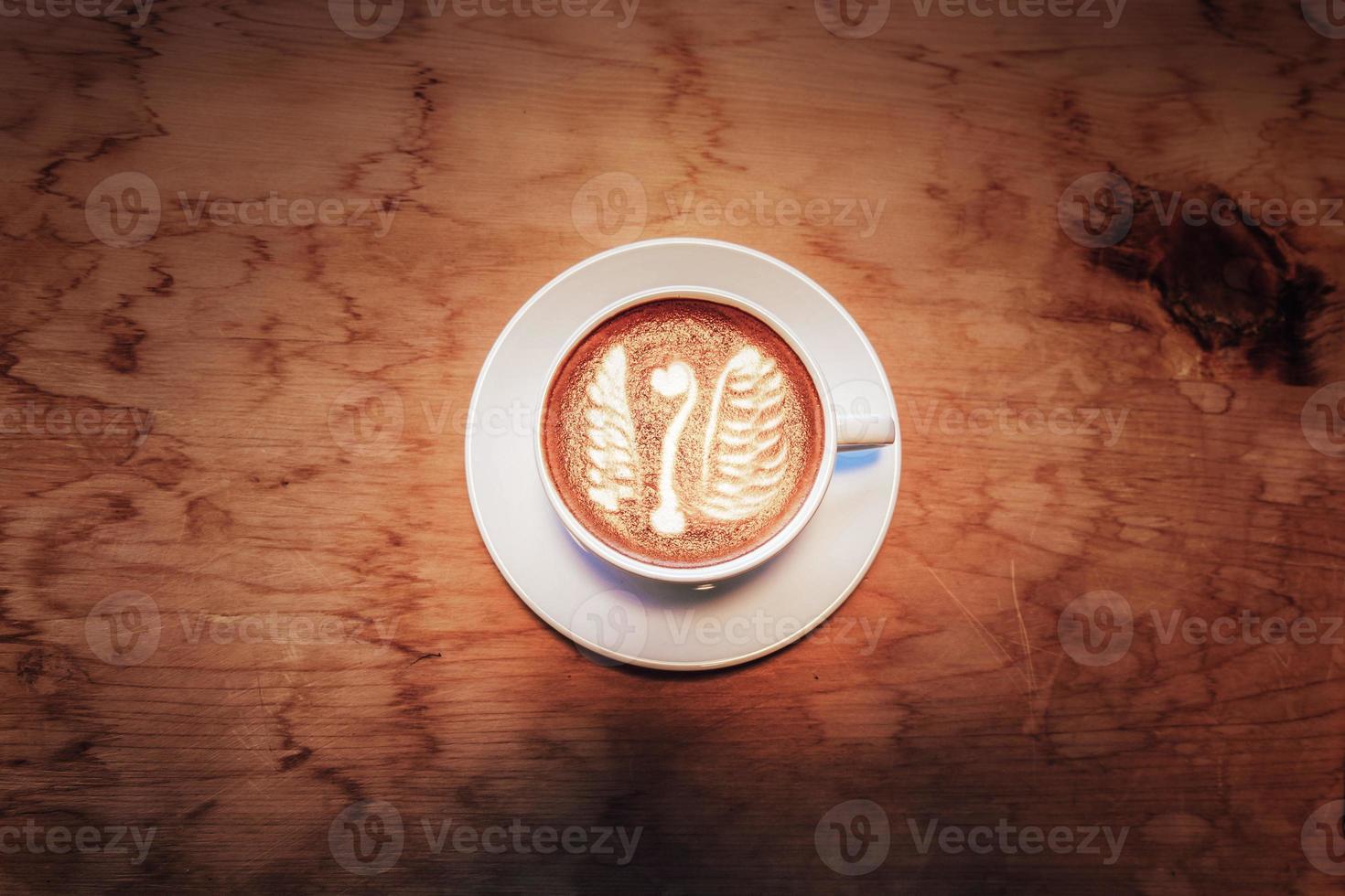 A latte cup decorated with white goose-shaped cream sits on a wooden table in a neon-lit cafe. photo