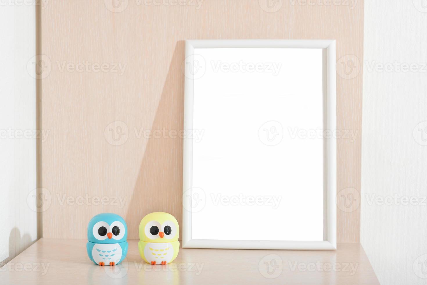 two little owl statues next to white empty frame on a bedside table in kids room. copy space for inscription photo