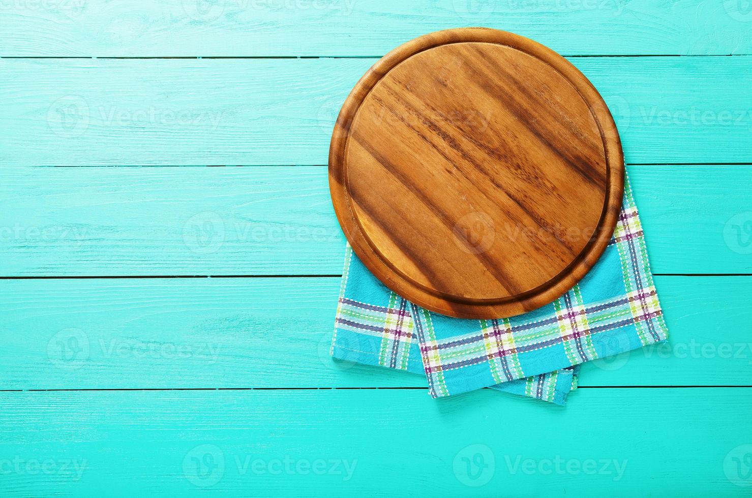 Plaid tablecloth and brown cutting board for pizza on blue wooden background. Top view and copy space. Mock up photo