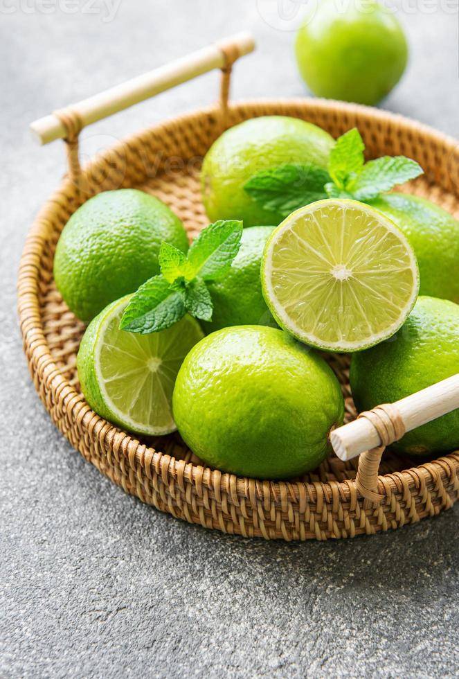 limas verdes con hojas de menta fresca en bandeja de mimbre foto