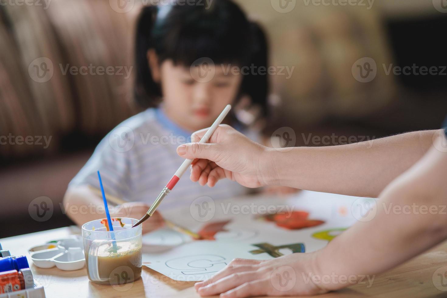 lindo bebé asiático sonriendo y su madre pintando con pinturas coloridas usando acuarela. chica asiática usando color de dibujo de pincel. concepto de estilo de vida de actividad del bebé. foto