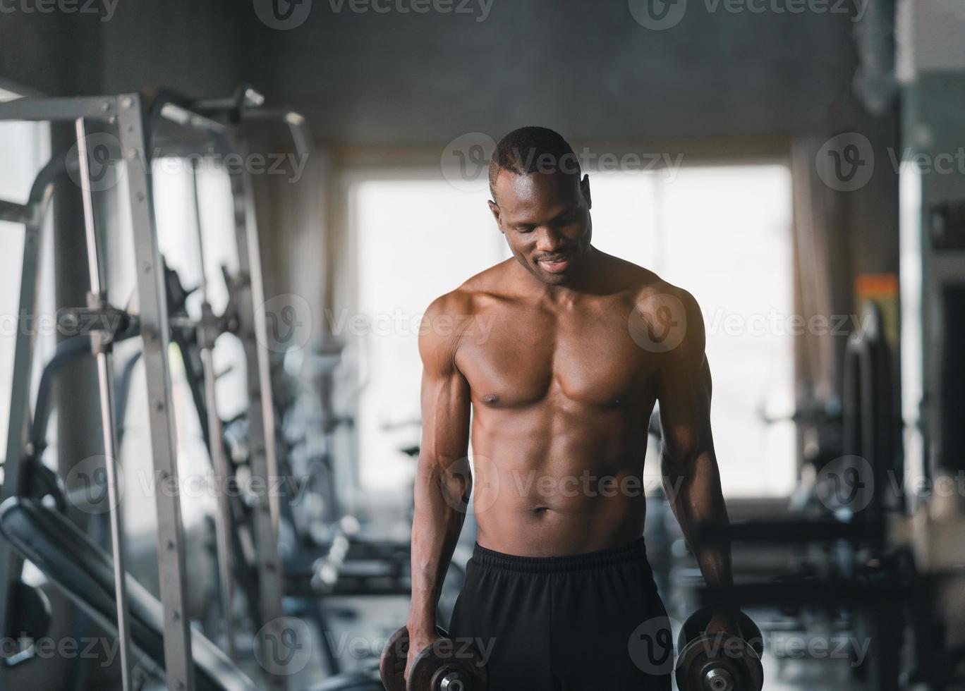 African sport man strong muscle working out excercise in weights with dumbbell at fitness room at the gym. Body building sport man fitness concept. photo