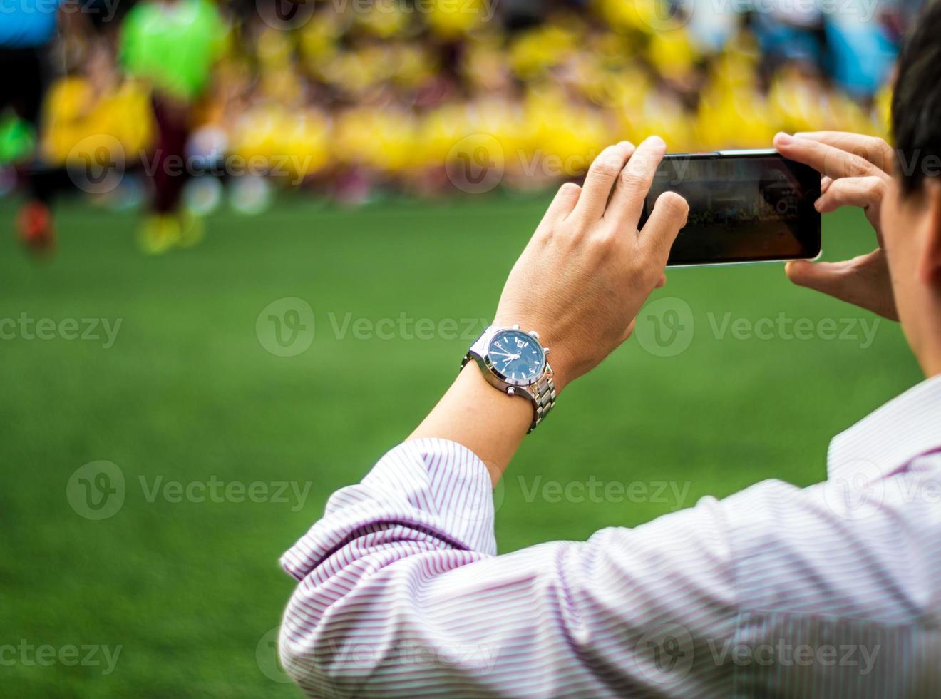 hombre con uniforme de trabajo mira y dispara competiciones de fútbol al lado del campo de fútbol foto