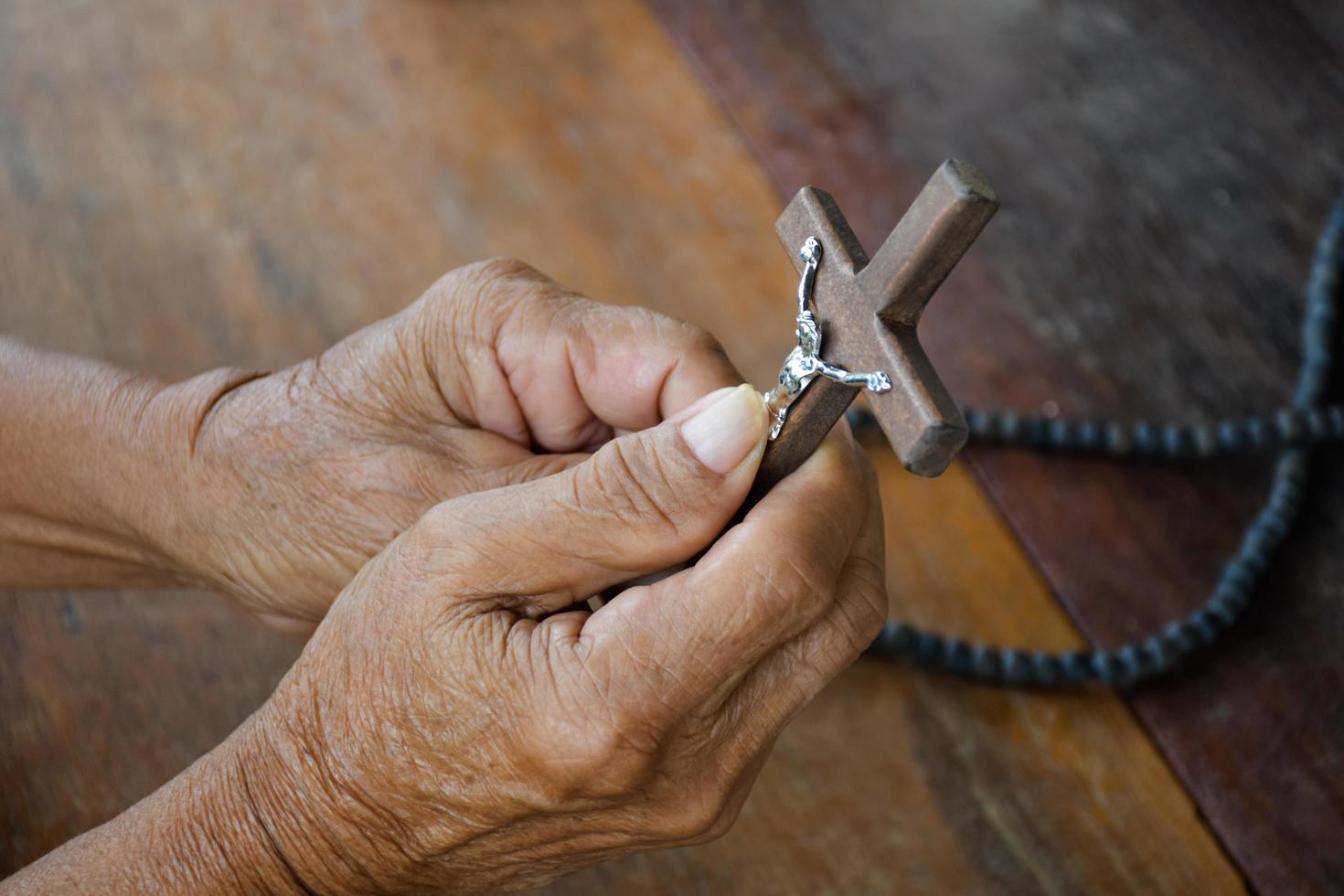 la cruz de madera cerrada que tiene una estatua de metal de jesús crucificado está en manos de un anciano católico asiático mientras reza en una iglesia local, enfoque suave y selectivo. foto