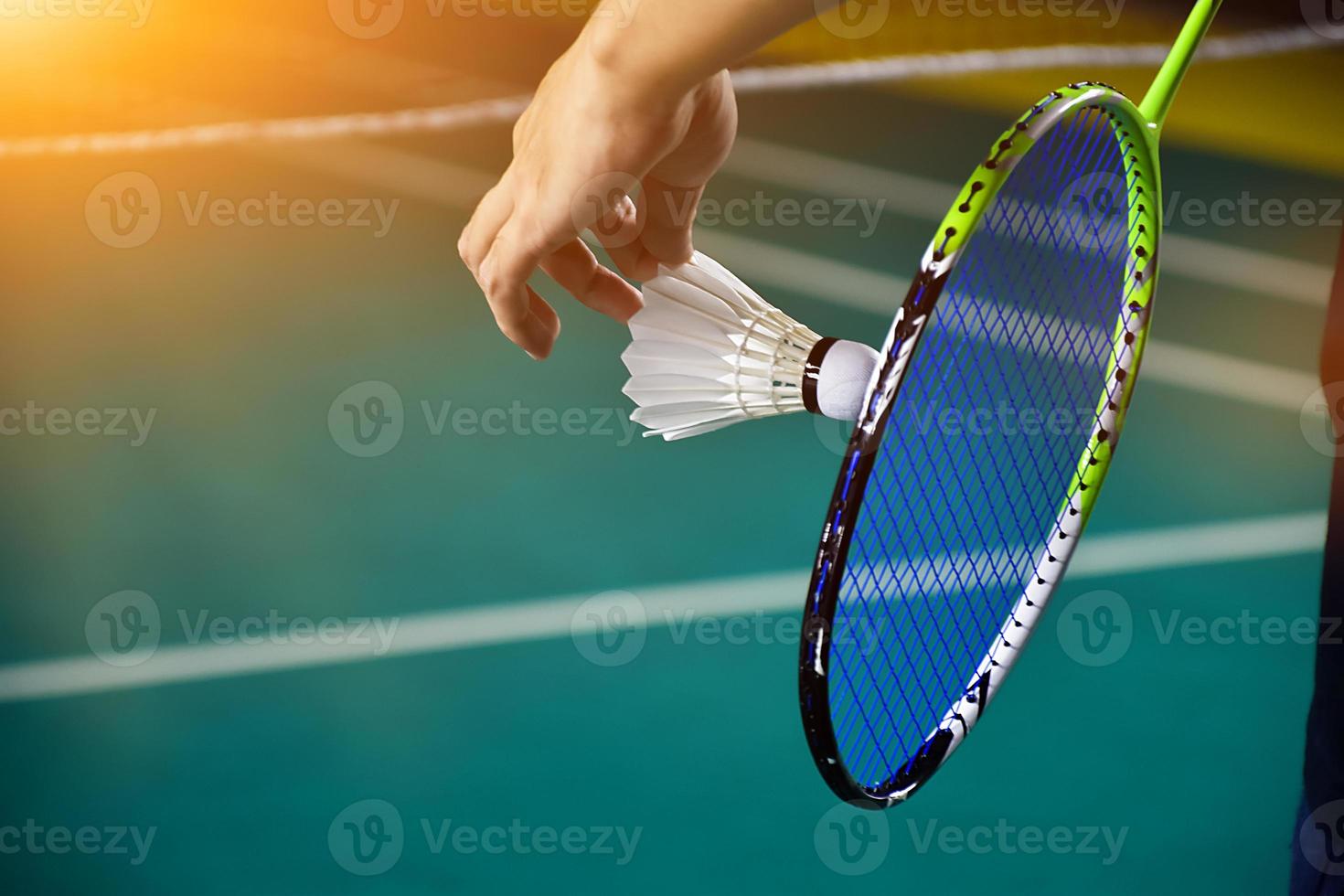 Cream white badminton shuttlecock and racket with neon light shading on green floor in indoor badminton court, blurred badminton background, copy space. photo
