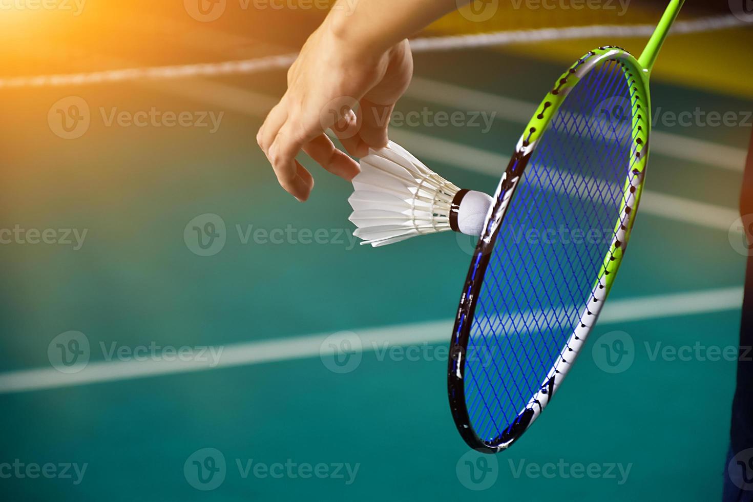 volante de bádminton blanco crema y raqueta con sombreado de luz de neón en el suelo verde en la cancha de bádminton cubierta, fondo de bádminton borroso, espacio para copiar. foto