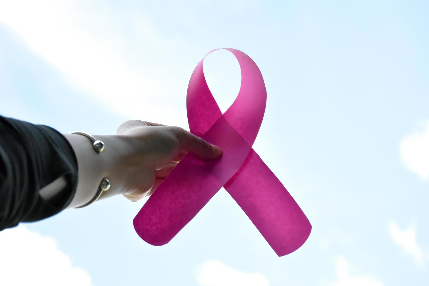 Pink paper ribbon holding in hands of female teenager to show and to call out all people around the world to support and to attend the breast cancer campaign of woman, soft and selective focus. photo