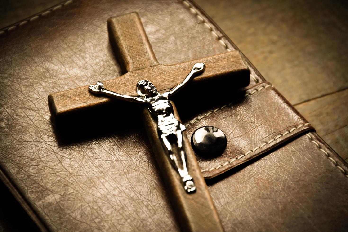 Closeup wooden cross which has a metal statue of crucified Jesus is on wooden table and near the notebook in a local church, soft and selective focus. photo