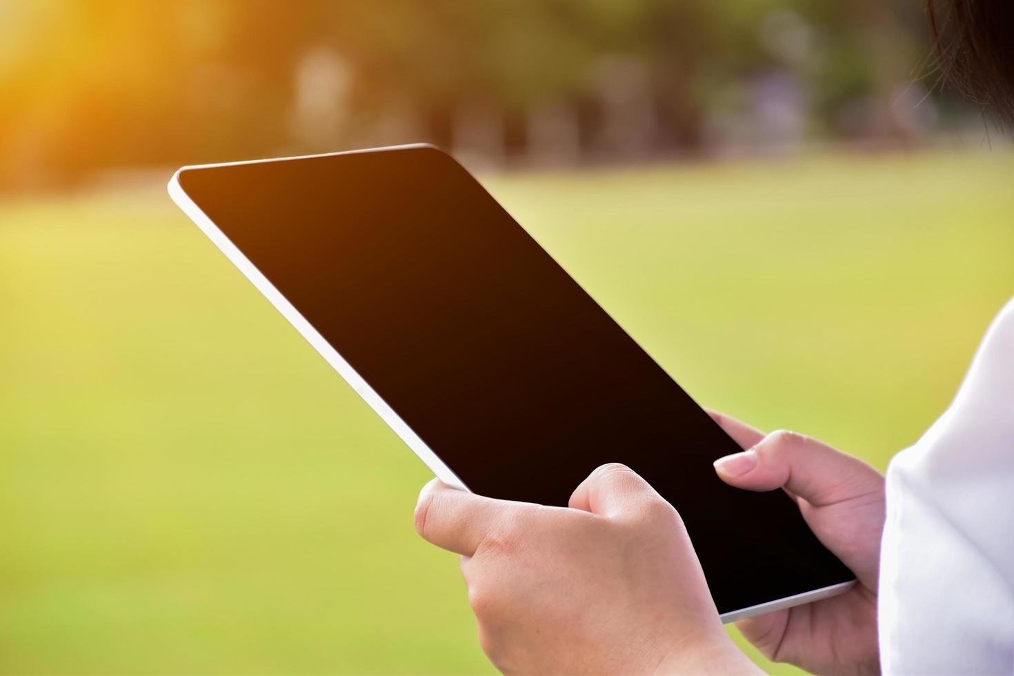 Black and blank touchscreen taplet in hands of woman, natural bokeh background, concept for using digital devices in daily life. photo
