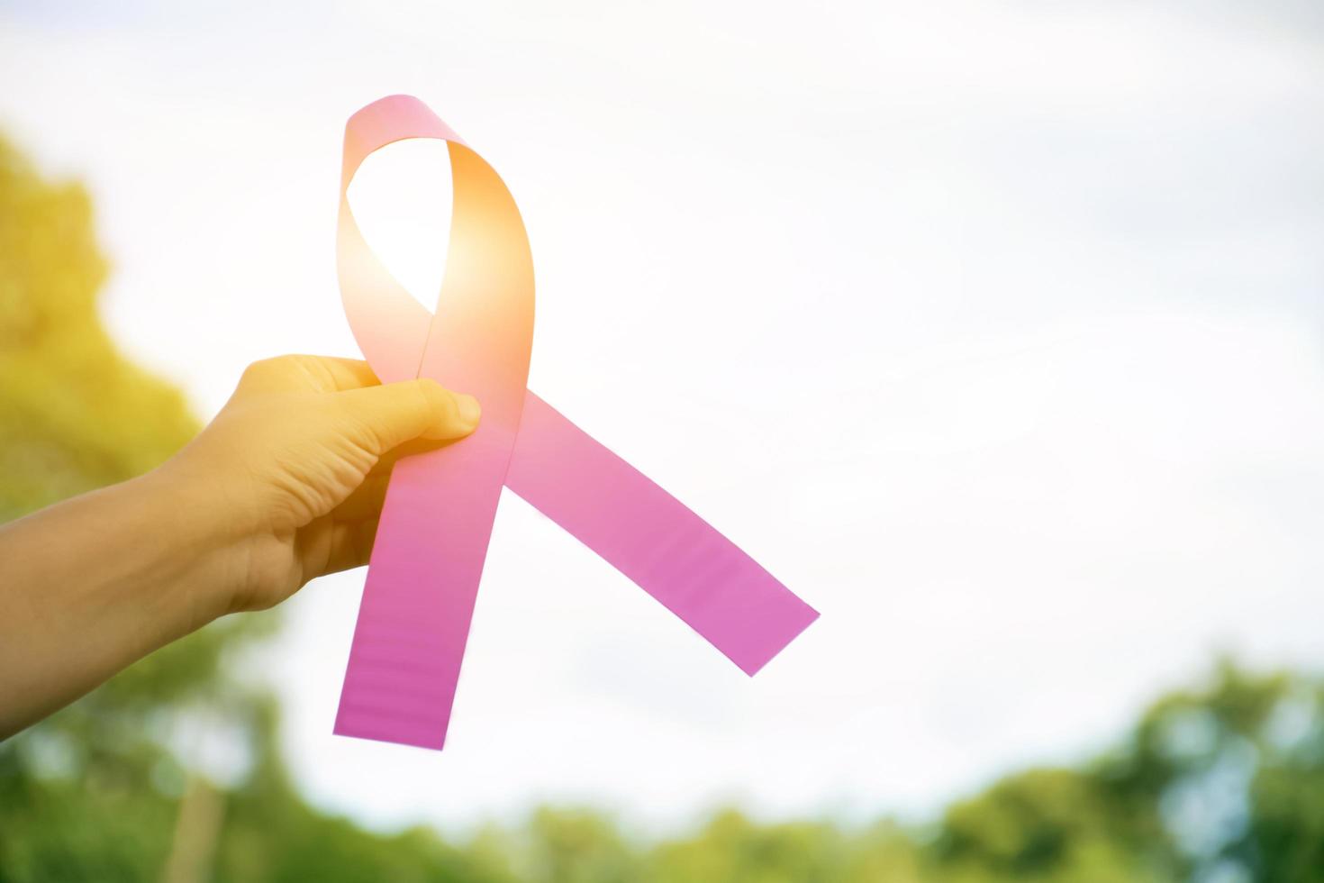 Pink paper ribbon holding in hands of female teenager to show and to call out all people around the world to support and to attend the breast cancer campaign of woman, soft and selective focus. photo