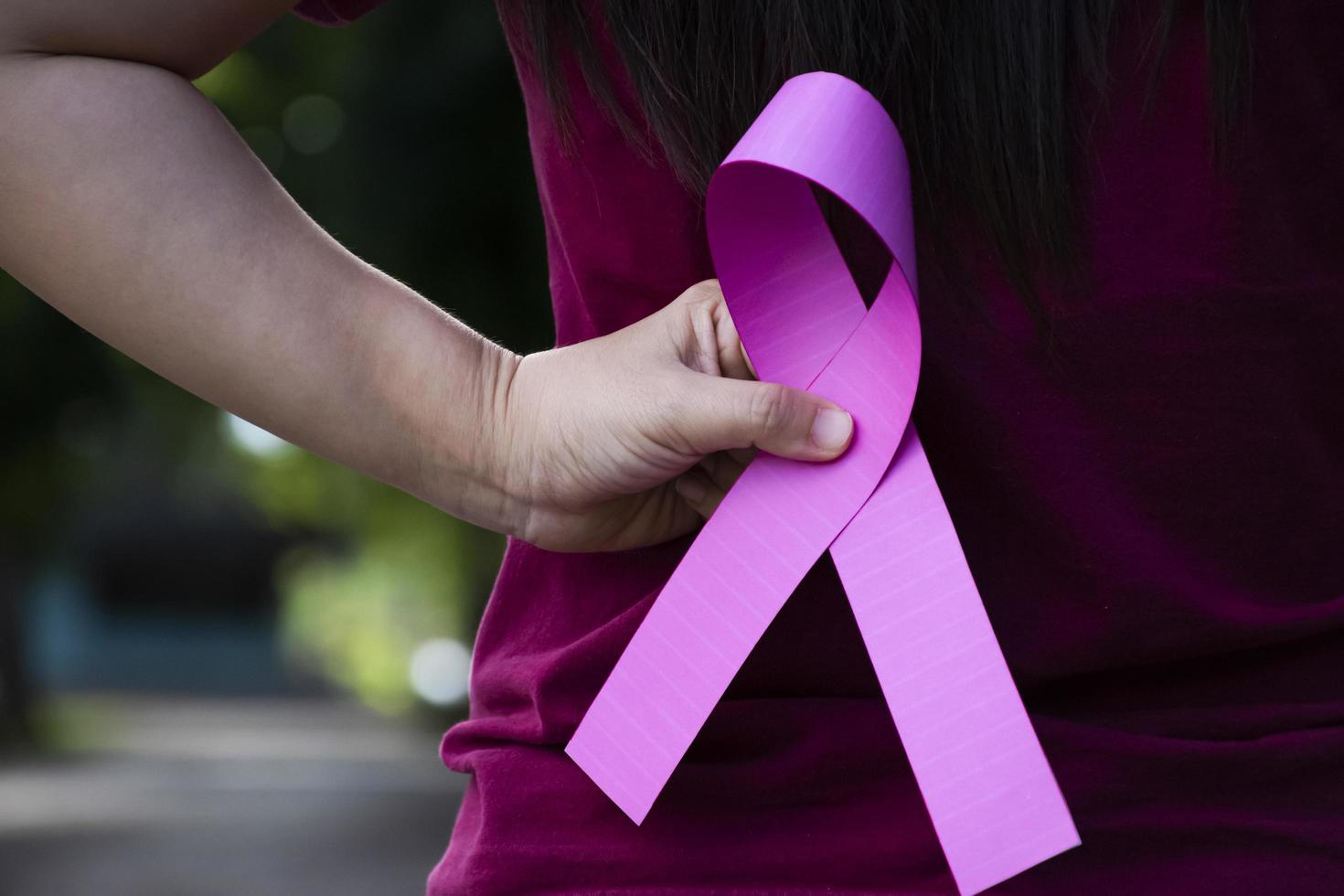 Pink paper ribbon holding in hands of female teenager to show and to call out all people around the world to support and to attend the breast cancer campaign of woman, soft and selective focus. photo