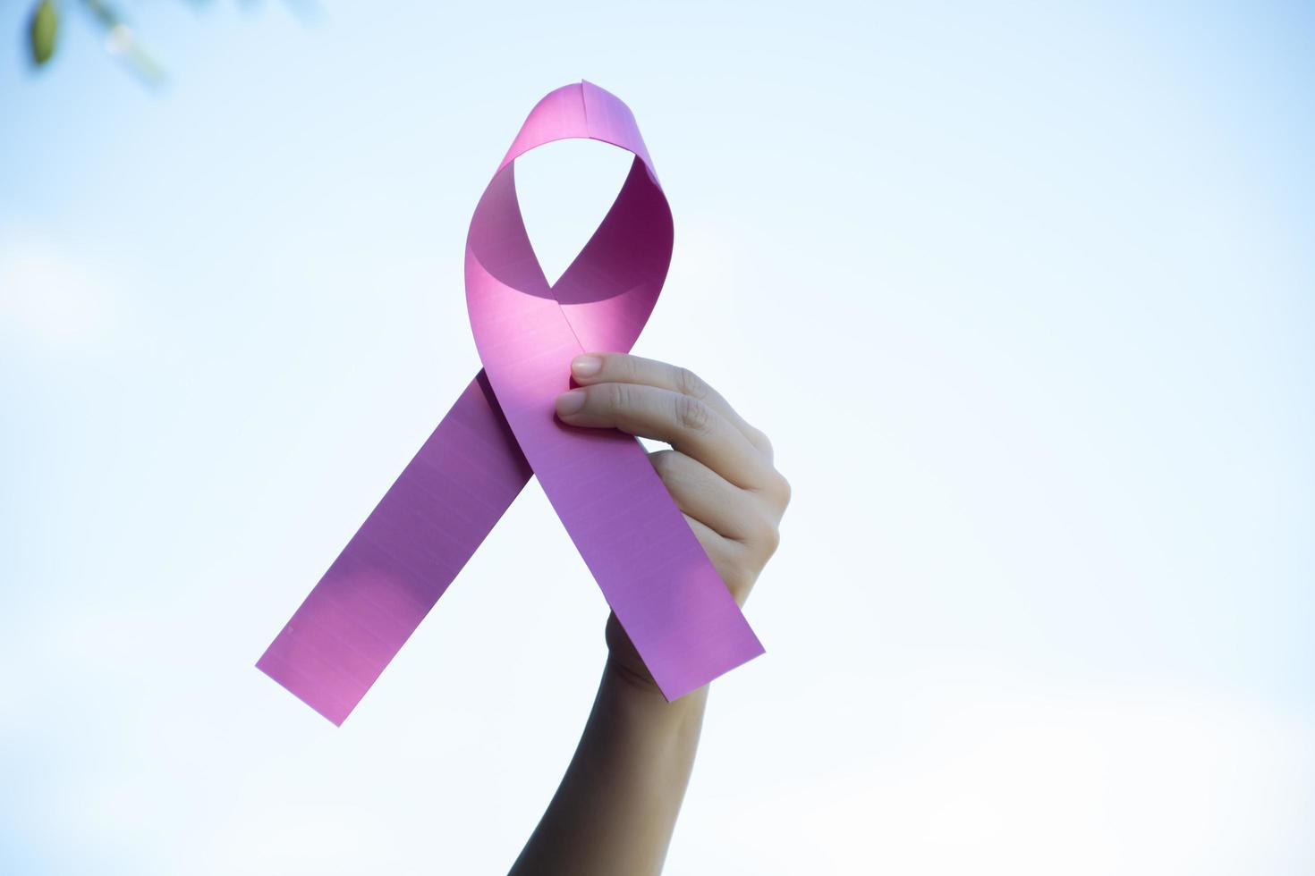 Pink paper ribbon holding in hands of female teenager to show and to call out all people around the world to support and to attend the breast cancer campaign of woman, soft and selective focus. photo