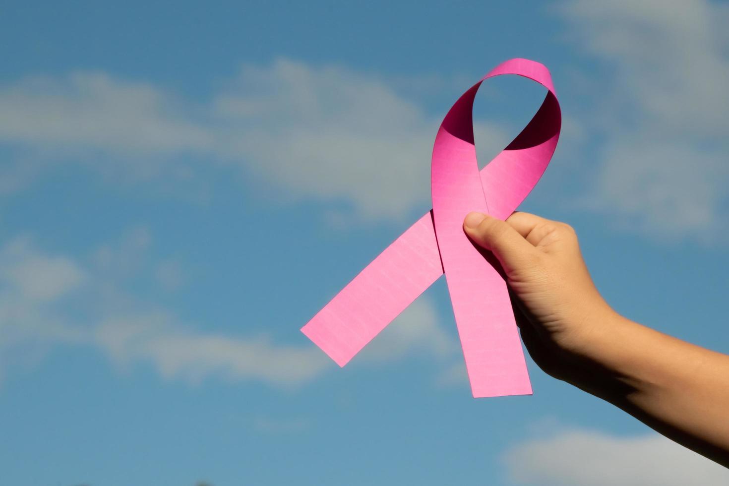 Pink paper ribbon holding in hands of female teenager to show and to call out all people around the world to support and to attend the breast cancer campaign of woman, soft and selective focus. photo