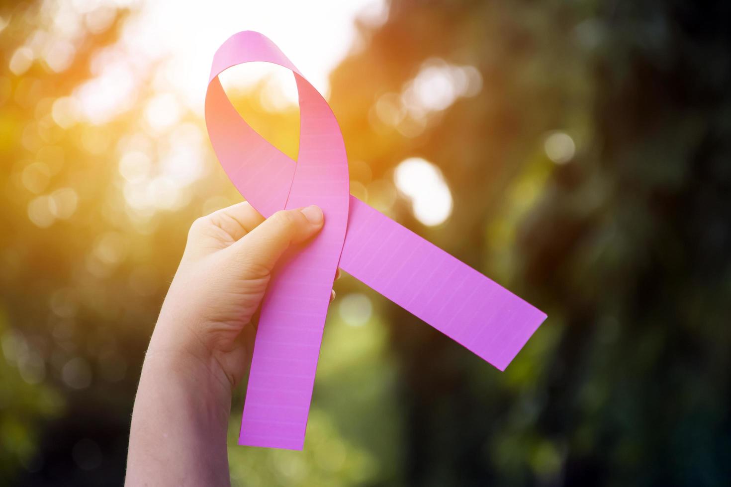 Pink paper ribbon holding in hands of female teenager to show and to call out all people around the world to support and to attend the breast cancer campaign of woman, soft and selective focus. photo