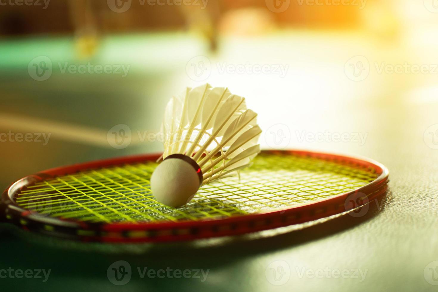 Cream white badminton shuttlecock and racket with neon light shading on green floor in indoor badminton court, blurred badminton background, copy space. photo