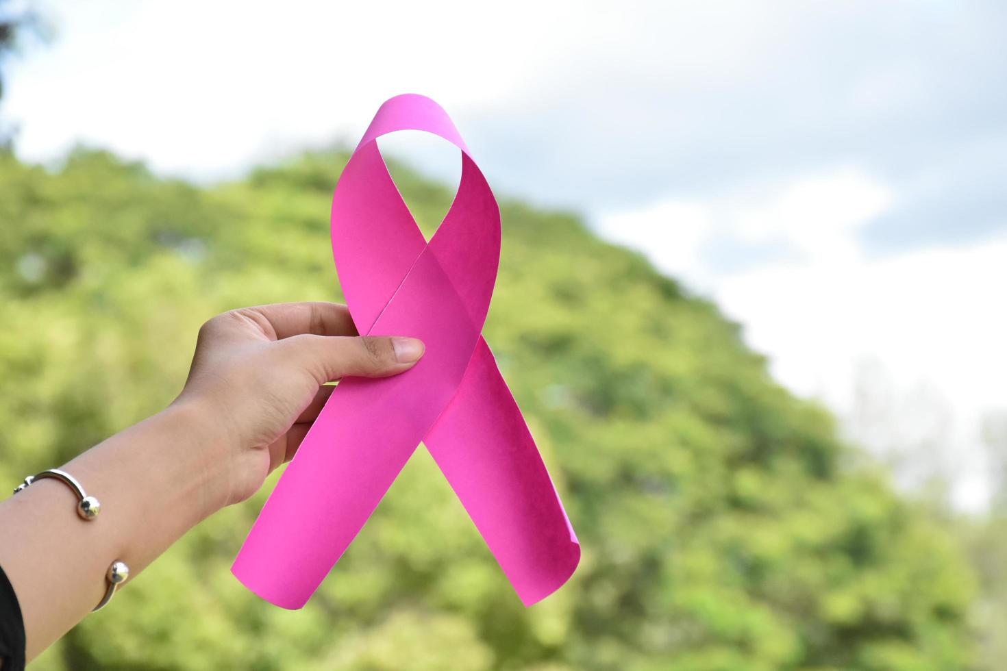 Pink paper ribbon holding in hands of female teenager to show and to call out all people around the world to support and to attend the breast cancer campaign of woman, soft and selective focus. photo