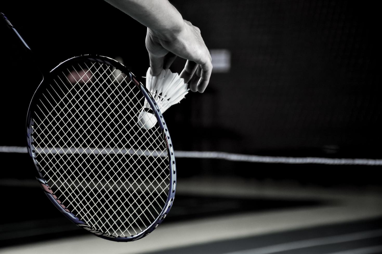 Cream white badminton shuttlecock and racket with neon light shading on green floor in indoor badminton court, blurred badminton background, copy space. photo