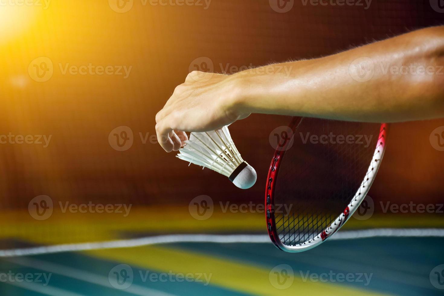 Badminton racket and old white shuttlecock holding in hands of player while serving it over the net ahead, blur badminton court background and selective focus. photo