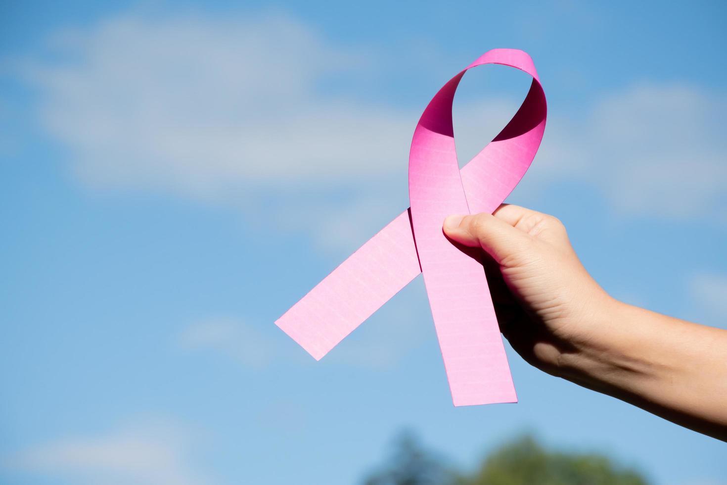 Pink paper ribbon holding in hands of female teenager to show and to call out all people around the world to support and to attend the breast cancer campaign of woman, soft and selective focus. photo