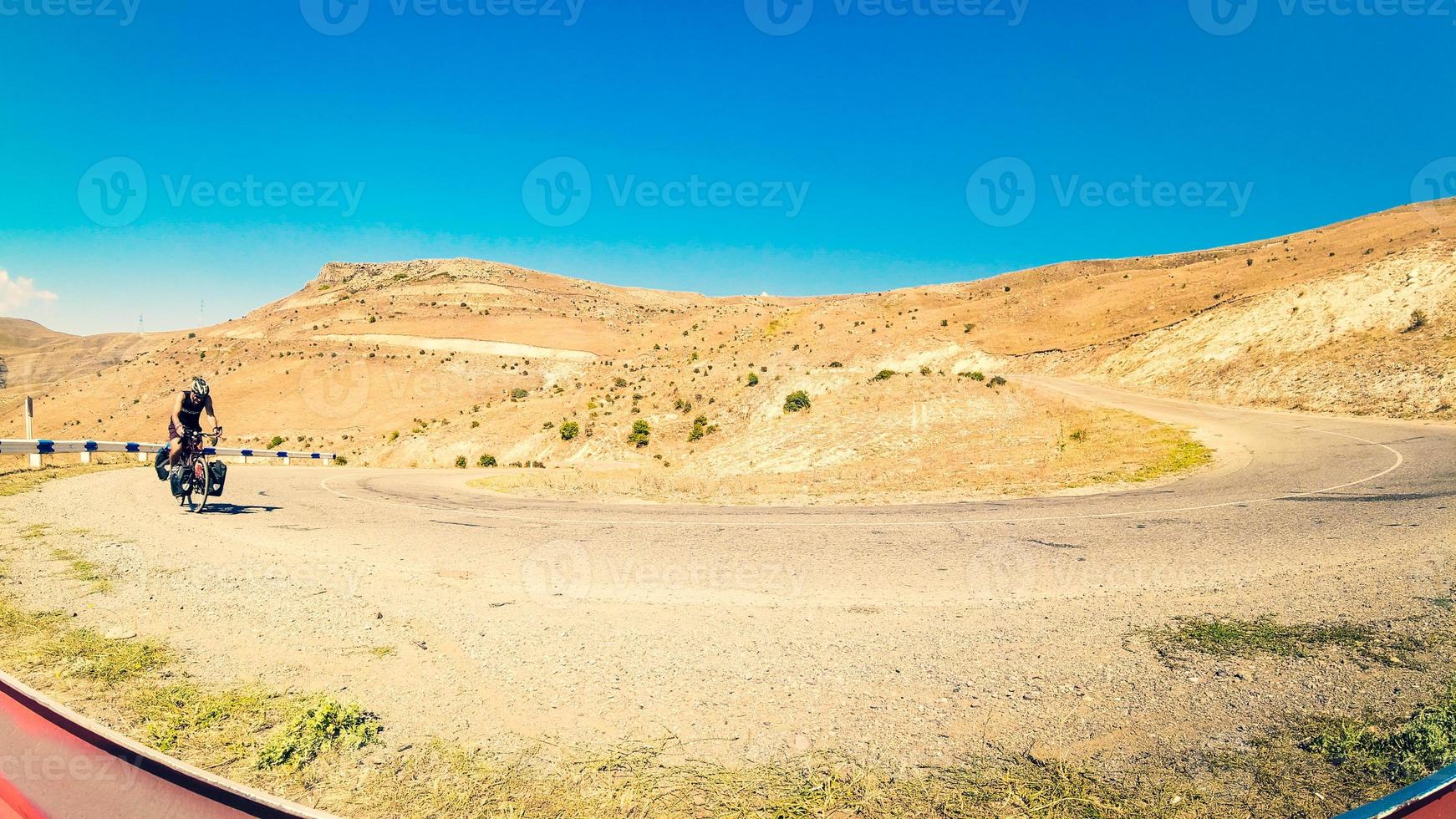 Fit young caucasian male person cycle with touring bicycle uphill in deserted road in caucasus mountains. Achievement , inspiration, challenge and determination concept photo