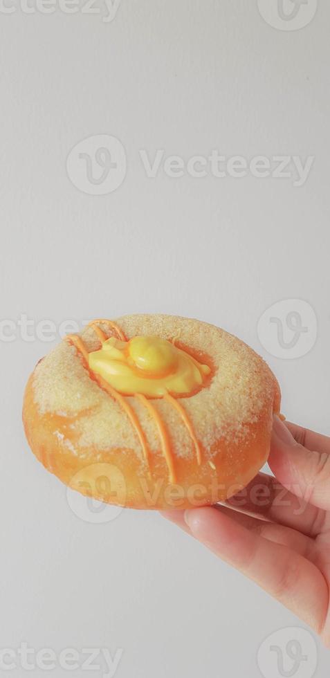 A hand is holding a donut with a unique taste. Shaped like a donut in general with a topping of an orange candy and orange candy flakes. photo