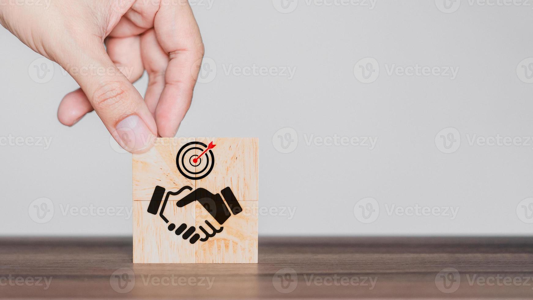 Hand put a handshake icon on wooden cubes block. Business partner or mergers and acquisitions concept. Business common goals and team collaboration. photo