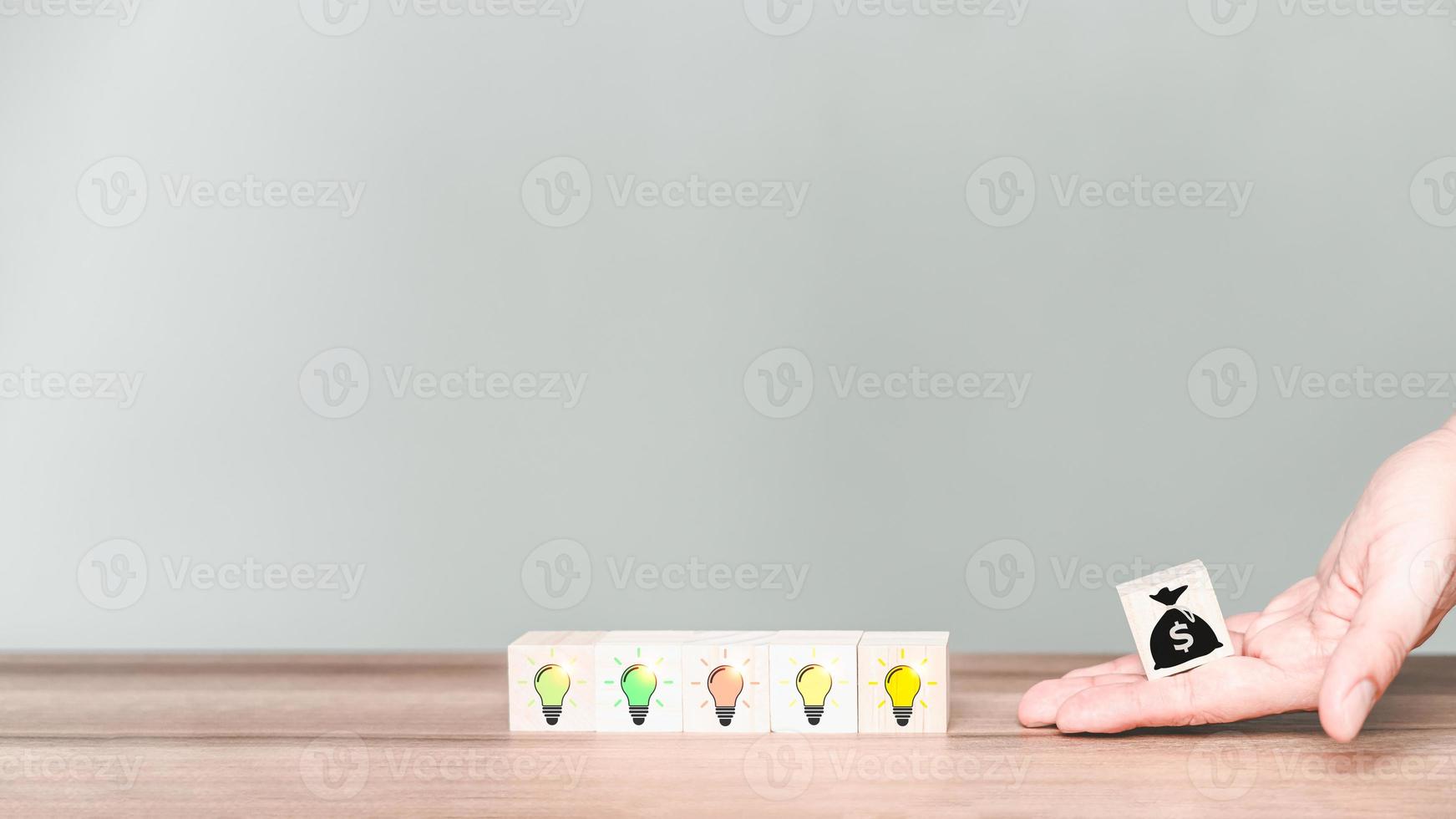 Adding business ideas to make money from online stores. Hand holding a money bag icon on wooden cube block with light bulb creative icon. Business growth idea. photo