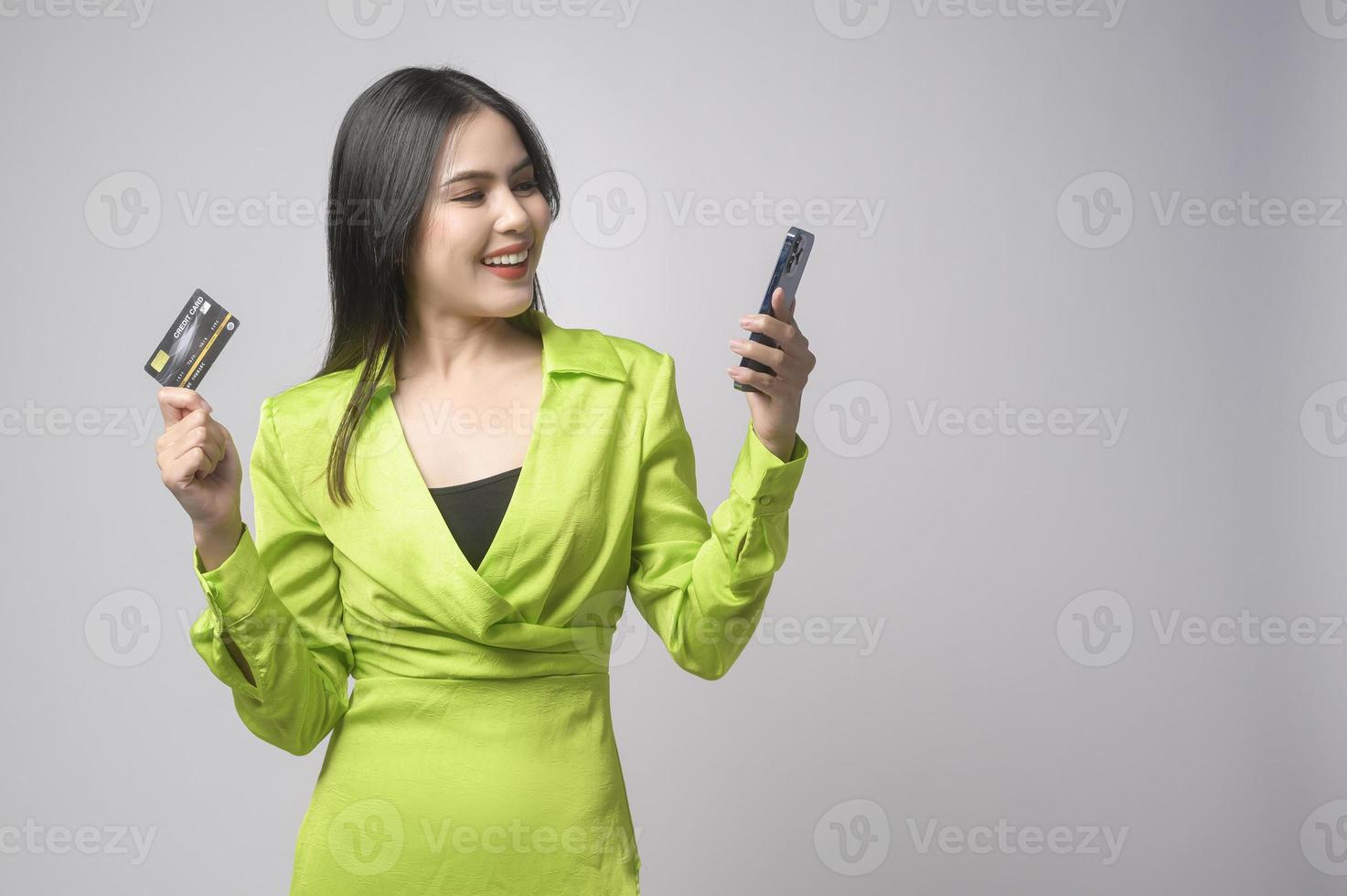 Beautiful woman holding credit card and smartphone over white background studio, shopping and finance concept. photo