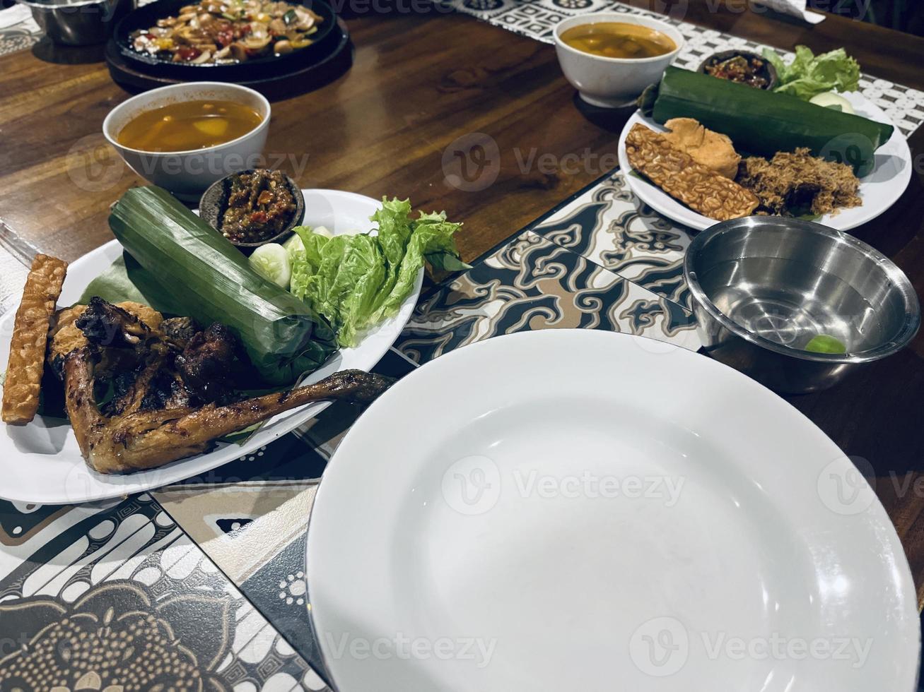 Indonesian cuisine or sundanese food called Nasi Timbel, Rice wrapped in banana leaves, served with fried chicken, tempeh, tofu, salted fish, chili sauce, lalap and sayur asem. photo