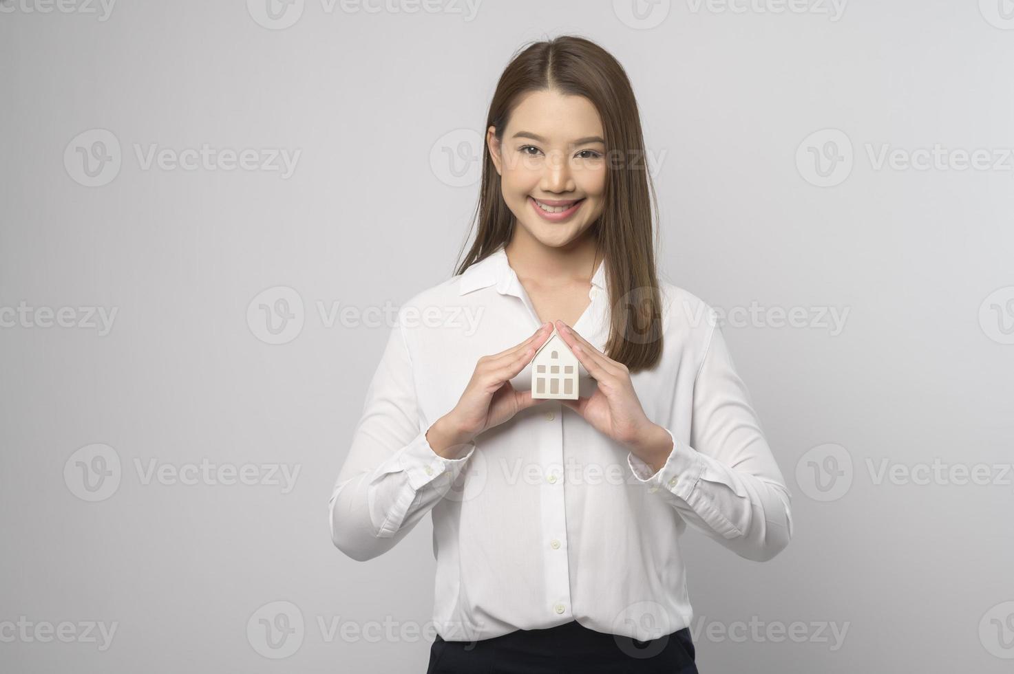 Young smiling woman holding small model house over white background studio photo