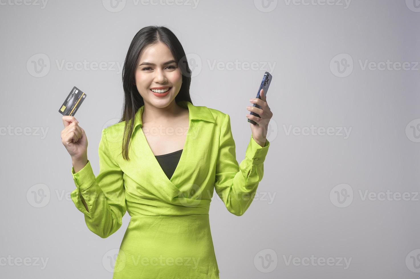 Beautiful woman holding credit card and smartphone over white background studio, shopping and finance concept. photo