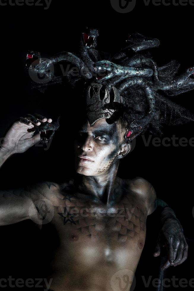 portrait of a man in the image of a basilisk with body art with a naked torso and a headdress in the form of a bunch of snakes photo