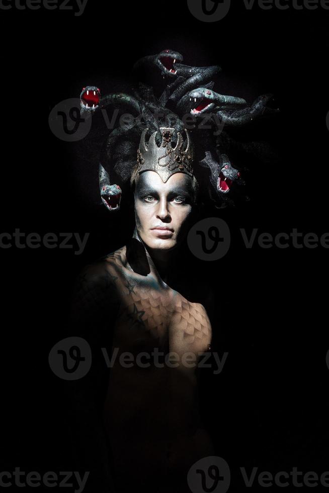 portrait of a man in the image of a basilisk with body art with a naked torso and a headdress in the form of a bunch of snakes photo