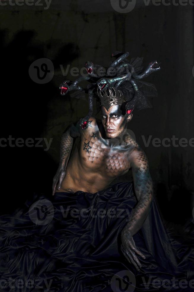 portrait of a man in the image of a basilisk with body art with a naked torso and a headdress in the form of a bunch of snakes photo