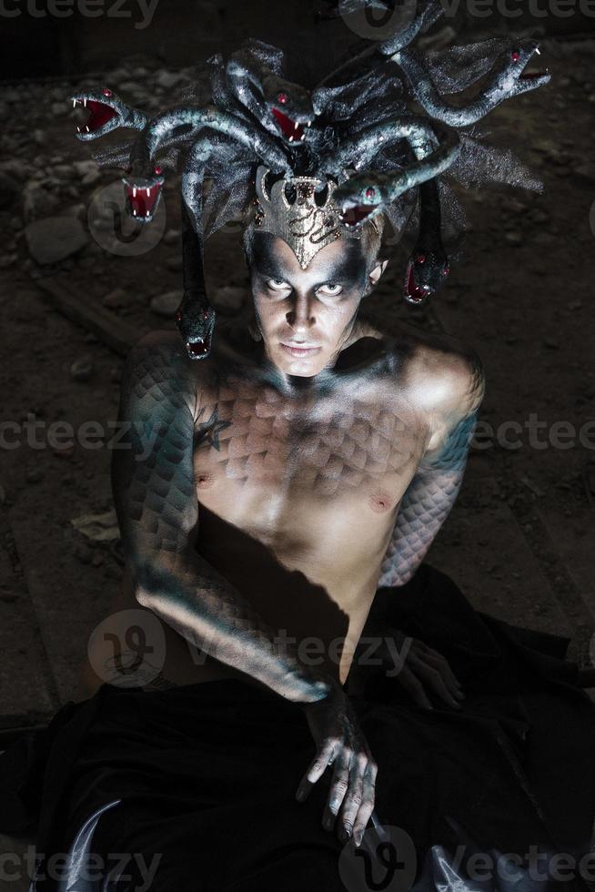 portrait of a man in the image of a basilisk with body art with a naked torso and a headdress in the form of a bunch of snakes photo