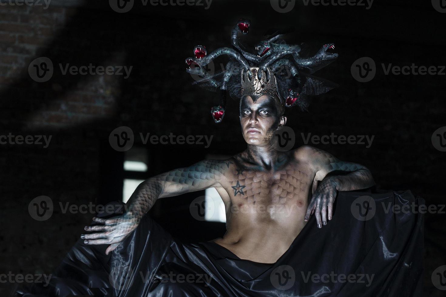 portrait of a man in the image of a basilisk with body art with a naked torso and a headdress in the form of a bunch of snakes photo