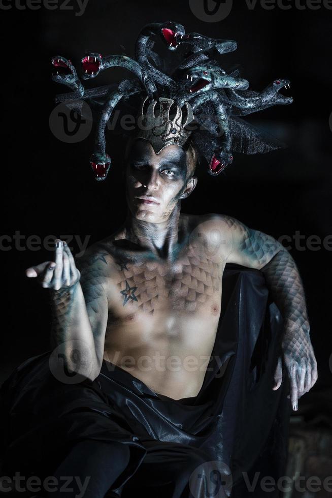 portrait of a man in the image of a basilisk with body art with a naked torso and a headdress in the form of a bunch of snakes photo